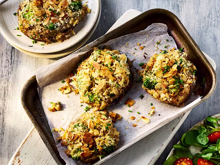 Four stuffed peppers topped served on a baking tray and a white dish with a side salad.