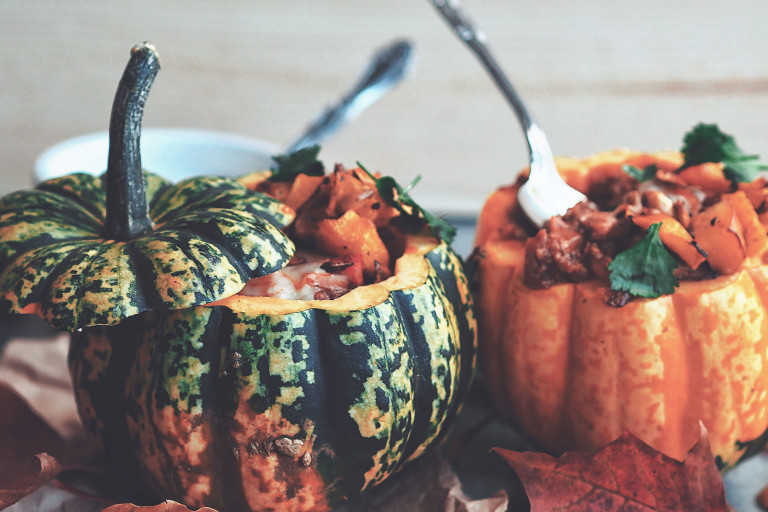 One green and one orange pumpkin, both topped and filled with vegetarian chili.
