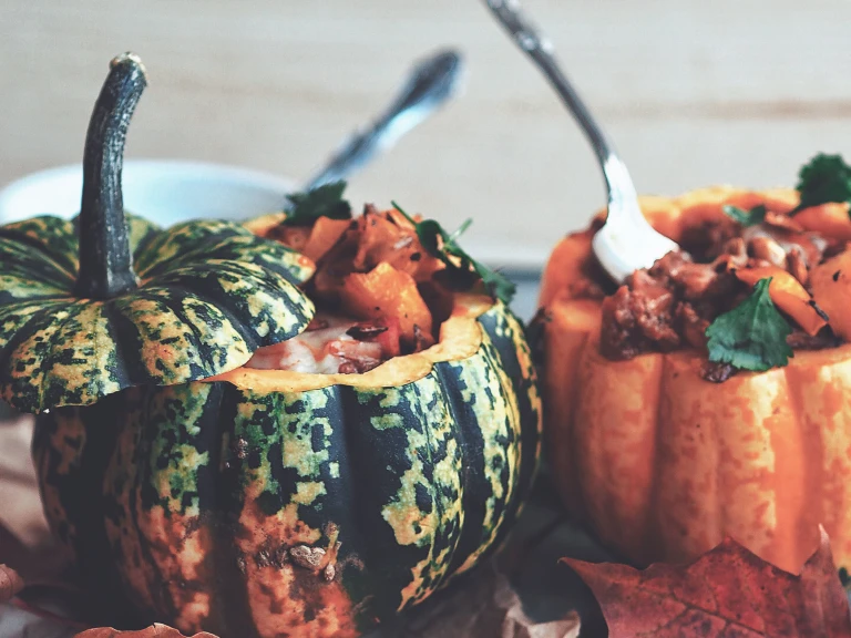 One green and one orange pumpkin, both topped and filled with vegetarian chili.