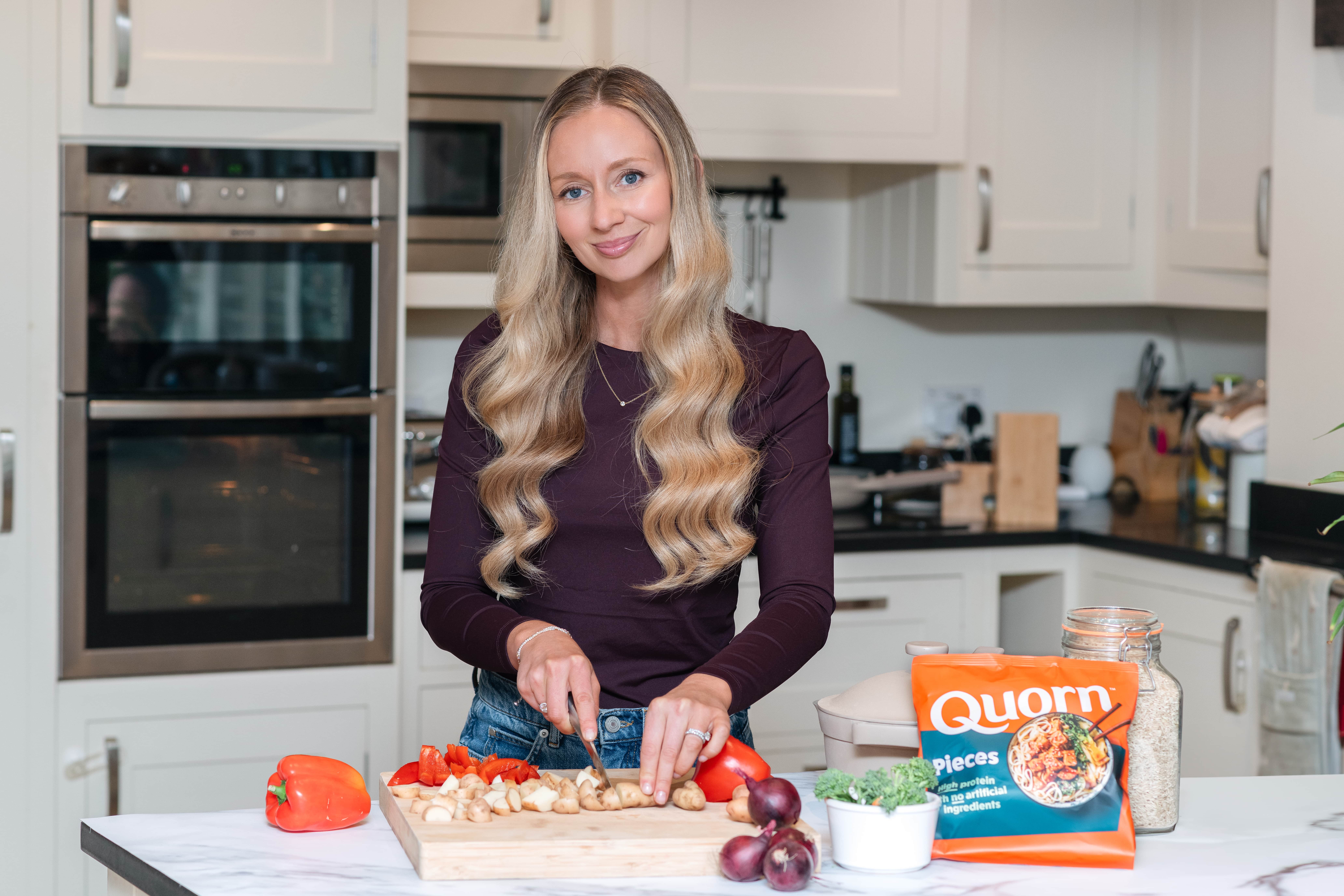 Image shows Rhiannon Lambert who is one of the leading UK nutritionists, at her home kitchen worktop chopping up vegetables on a chopping board with a pack of Quorn Pieces at the side.