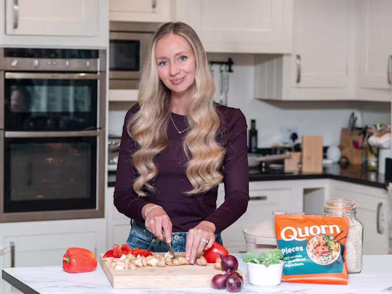 Image shows Rhiannon Lambert who is one of the leading UK nutritionists, at her home kitchen worktop chopping up vegetables on a chopping board with a pack of Quorn Pieces at the side.