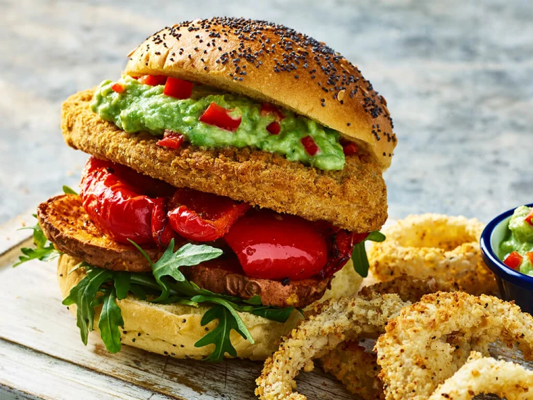 Two Quorn Crunchy Filet Cajun Burgers with onion rings on a board with a sweat pea guacamole in a bowl on the side