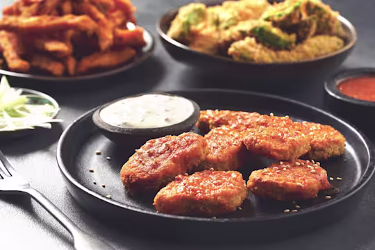 A plate of Quorn Vegan Buffalo Nuggets with Blue Cheese Sauce on a table containing homemade fries and crispy avocado wings.