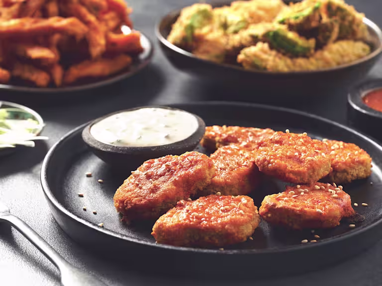 A black plate of Quorn Buffalo Nuggets with a ramekin of vegan blue cheese sauce on the side.