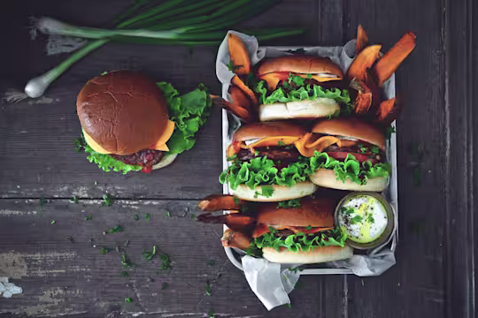4 Quorn Quarter Pounders in buns served on a tray with sweet potato fries and a pot of mayonnaise with one burger on the table