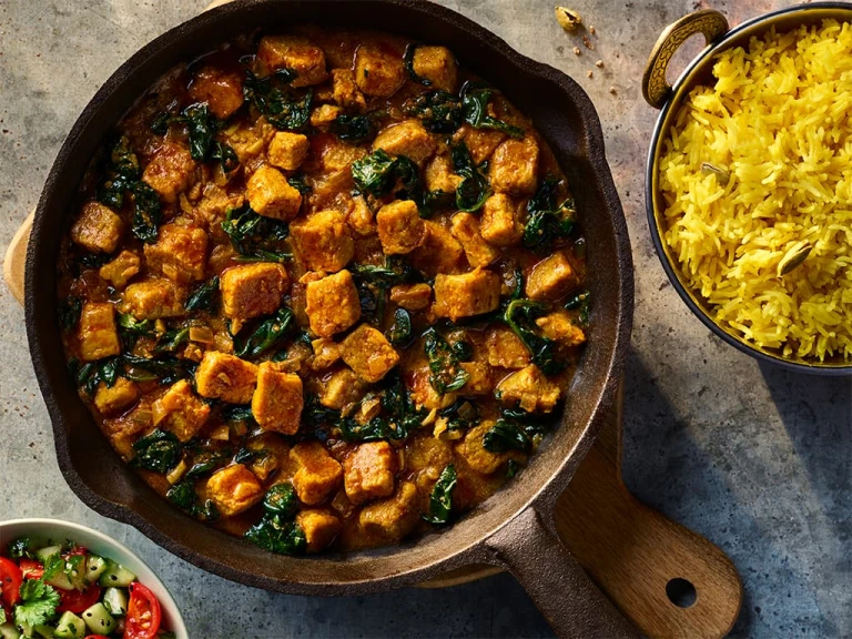 Vegetarian Chicken Saag made using Quorn Pieces served in a dark dish with a side of rice.