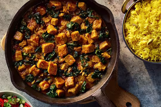 Vegetarian Chicken Saag made using Quorn Pieces served in a dark dish with a side of rice.