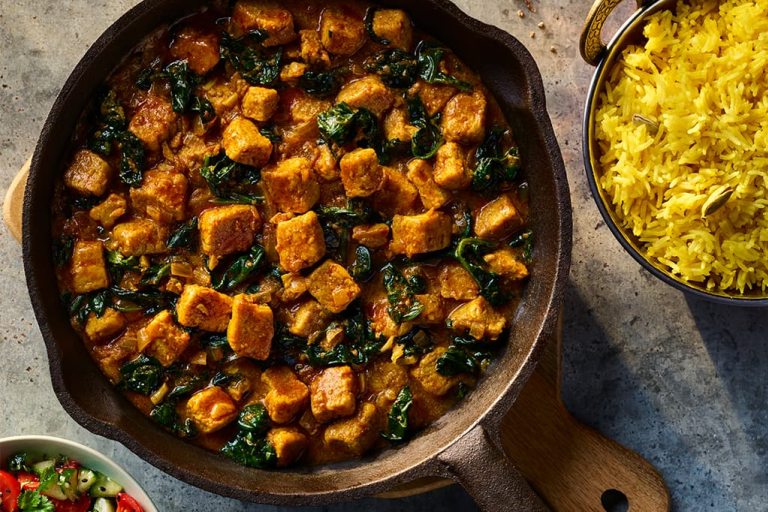 Vegetarian Chicken Saag made using Quorn Pieces served in a dark dish with a side of rice.