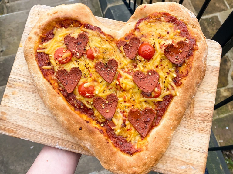 Heart pizza with heart shaped pepperoni served on a wooden board.