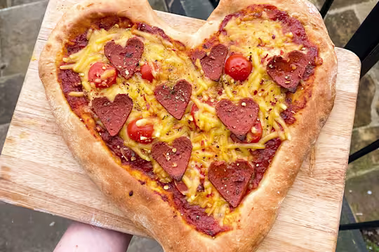 Heart pizza with heart shaped pepperoni served on a wooden board.
