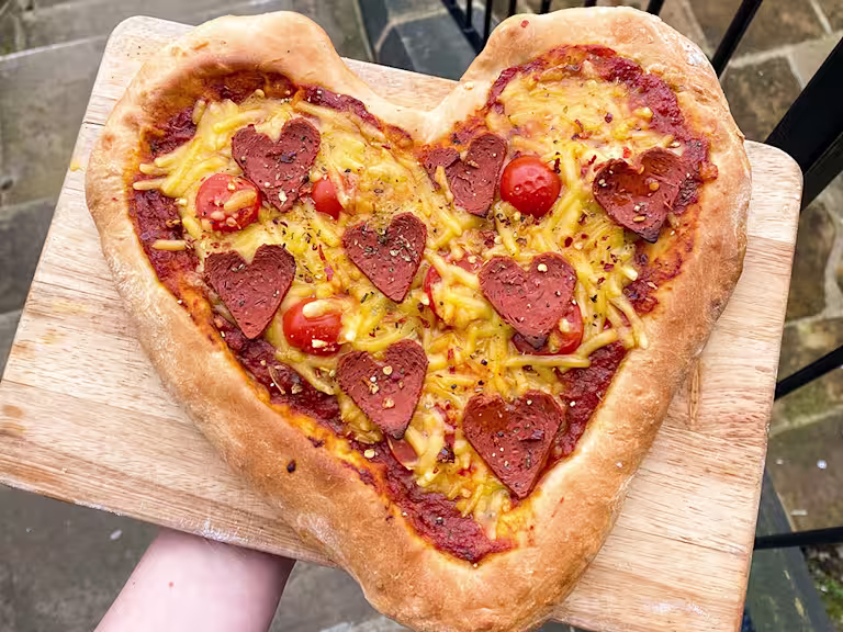 Heart pizza with heart shaped pepperoni served on a wooden board.