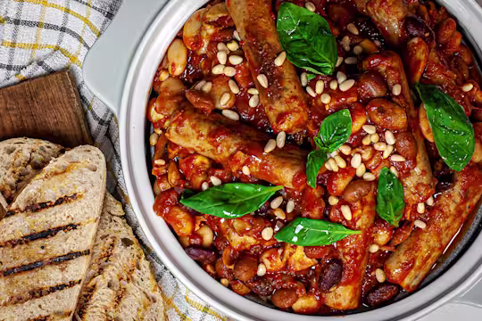 Tuscan sausage on bean stew in a bowl with charred bread on the side