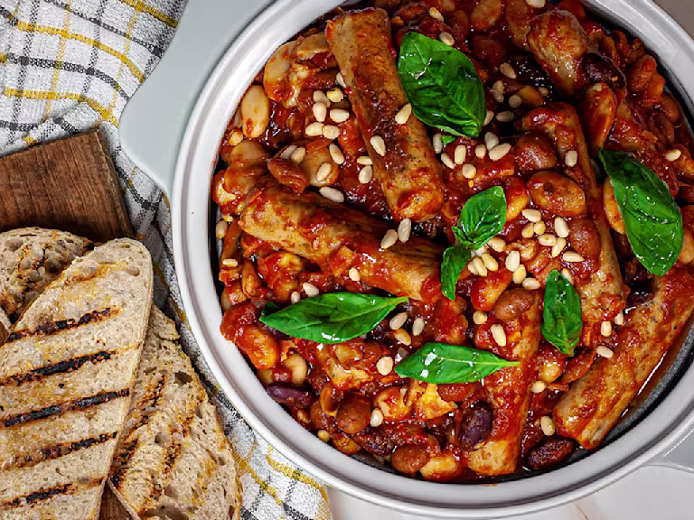 Tuscan sausage on bean stew in a bowl with charred bread on the side