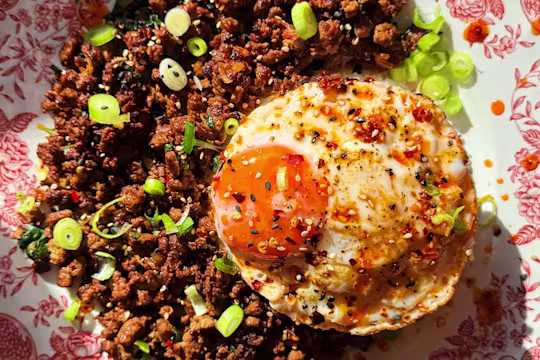 A bowl of Vegetarian Pad Kra Pao with Quorn Mince and garlic cloves, shallots, ginger, basil, sesame seeds and a fried egg on top.
