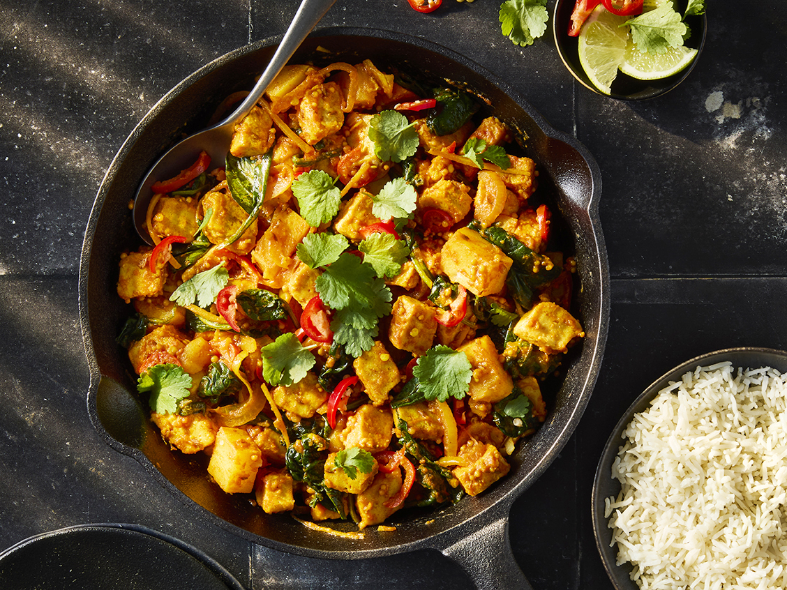 A vegetarian Saag Aloo with Quorn Pieces and potatoes, onion, red chilli, spinach, coriander leaves and white rice in a black bowl.