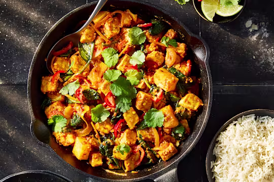 A vegetarian Saag Aloo with Quorn Pieces and potatoes, onion, red chilli, spinach, coriander leaves and white rice in a black bowl.