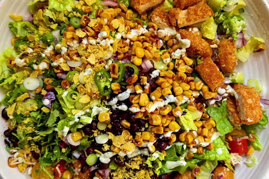 Salad with Quorn Cheesy Nacho Nuggs, sweetcorn, lettuce, green pepper, tomatoes and crushed tortilla chips on a white plate