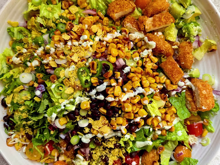 Salad with Quorn Cheesy Nacho Nuggs, sweetcorn, lettuce, green pepper, tomatoes and crushed tortilla chips on a white plate