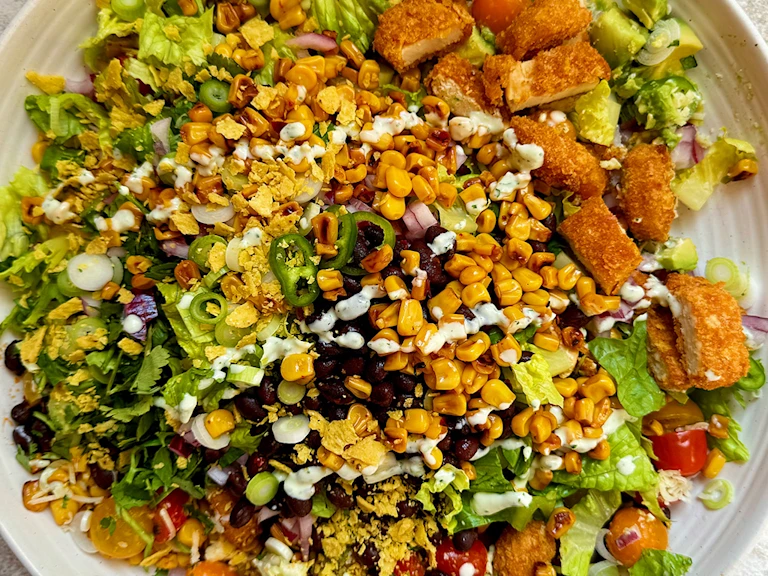 Salad with Quorn Cheesy Nacho Nuggs, sweetcorn, lettuce, green pepper, tomatoes and crushed tortilla chips on a white plate