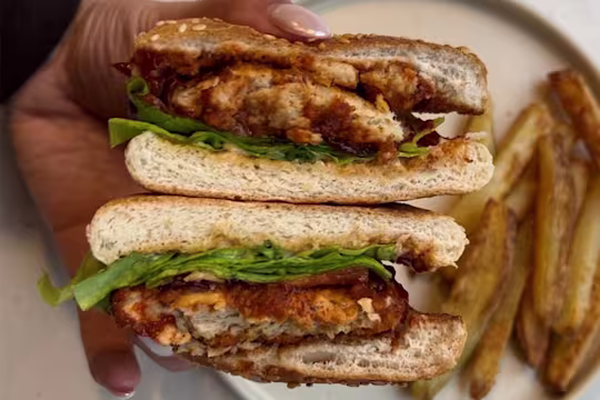 Cross section of Quorn Crunchy Fillet Burger coated in BBQ sauce in a seeded burger bun with lettuce, tomato and mayonnaise.
