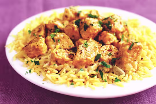 Quorn Pieces in a korma sauce on a white plate with yellow rice and coriander garnish.