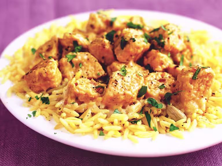 Quorn Pieces in a korma sauce on a white plate with yellow rice and coriander garnish.
