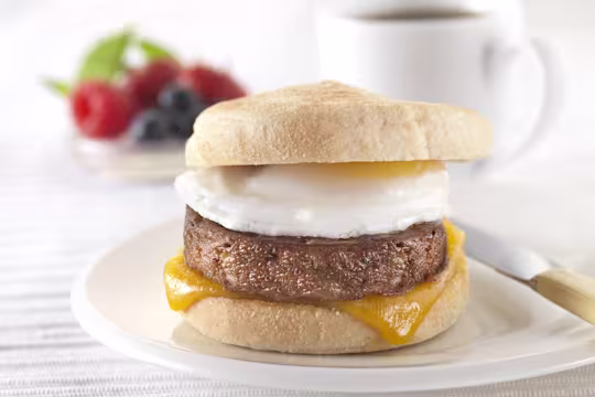 A muffin filled with a Quorn Sausage Patty, a slice of melted cheese, and a fried egg on a white plate.