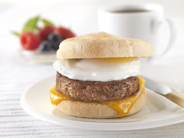 A muffin filled with a Quorn Sausage Patty, a slice of melted cheese, and a fried egg on a white plate.