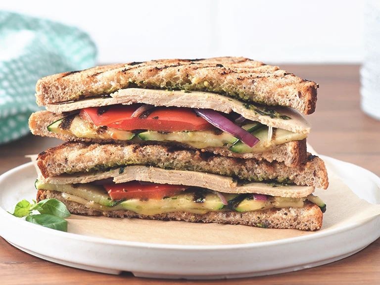 Veggie lunch idea made with Quorn Chicken Free Slices, pesto and grilled vegetables in a sandwich served on a white plate