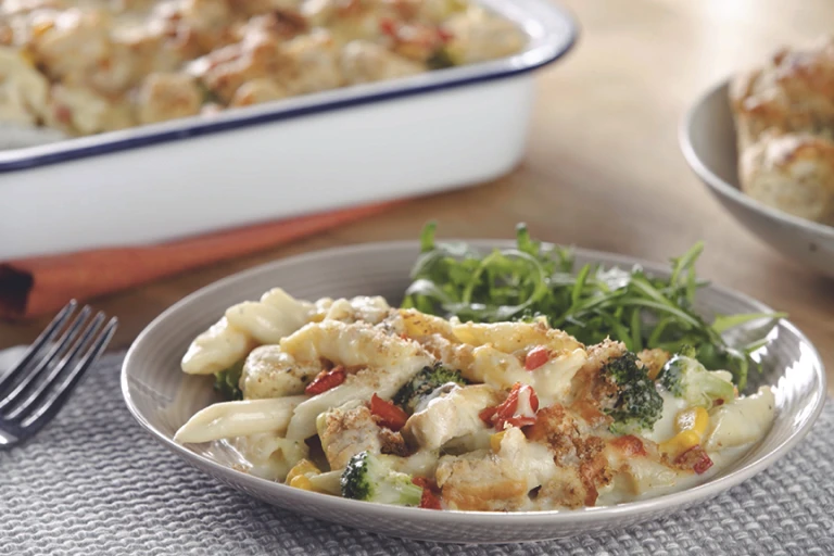 A bowl of penne pasta bake with Quorn Pieces, broccoli, and sweetcorn topped with cheese and breadcrumbs with a salad on the side.