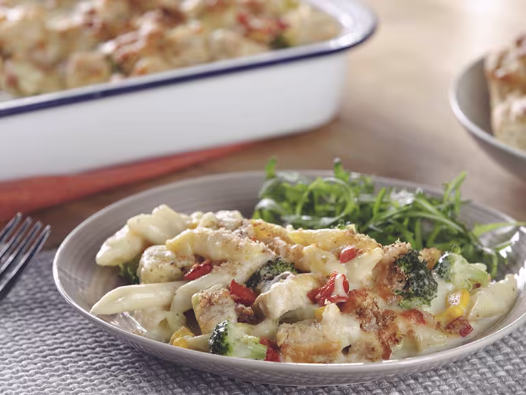 A bowl of penne pasta bake with Quorn Pieces, broccoli, and sweetcorn topped with cheese and breadcrumbs with a salad on the side.