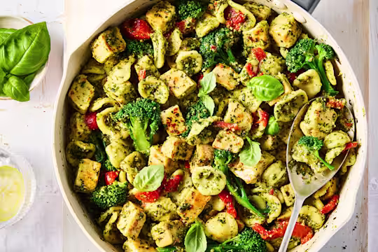 Quorn Chicken Pieces with pesto, broccoli and pasta with chopped tomatoes in a saucepan with a serving spoon.