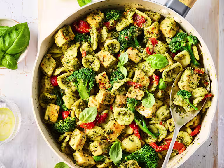 Quorn Chicken Pieces with pesto, broccoli and pasta with chopped tomatoes in a saucepan with a serving spoon.
