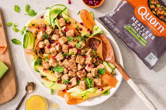 A salad with ribbons of cucumber, papaya, and carrots topped with mint, pomegranate seeds, and Quorn Pieces.
