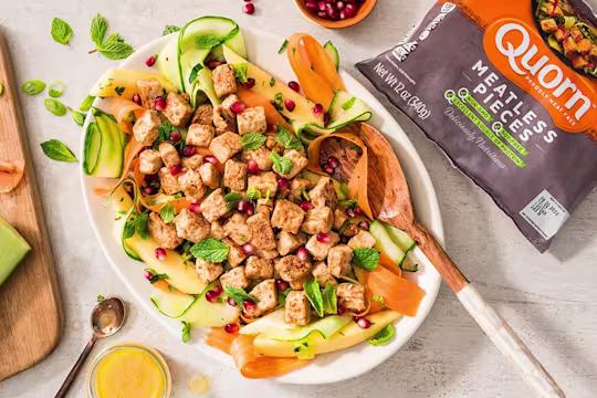 A salad with ribbons of cucumber, papaya, and carrots topped with mint, pomegranate seeds, and Quorn Pieces.
