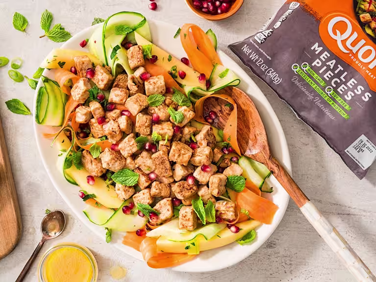 A salad with ribbons of cucumber, papaya, and carrots topped with mint, pomegranate seeds, and Quorn Pieces.