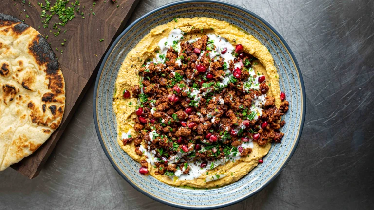 A Crispy Harissa Quorn Vegetarian Mince With Squash Hummus topped with pomegranate seeds served in a blue dish.