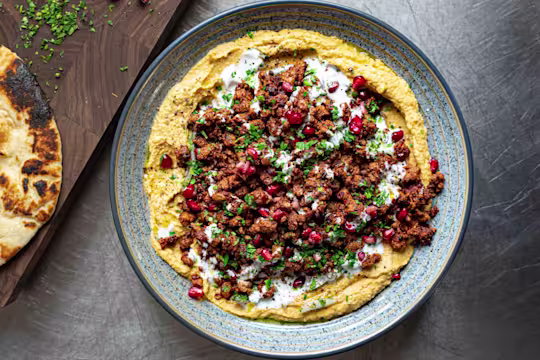 A Crispy Harissa Quorn Vegetarian Mince With Squash Hummus topped with pomegranate seeds served in a blue dish.