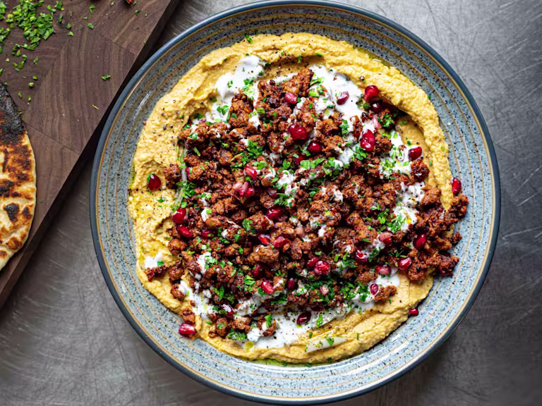 A Crispy Harissa Quorn Vegetarian Mince With Squash Hummus topped with pomegranate seeds served in a blue dish.