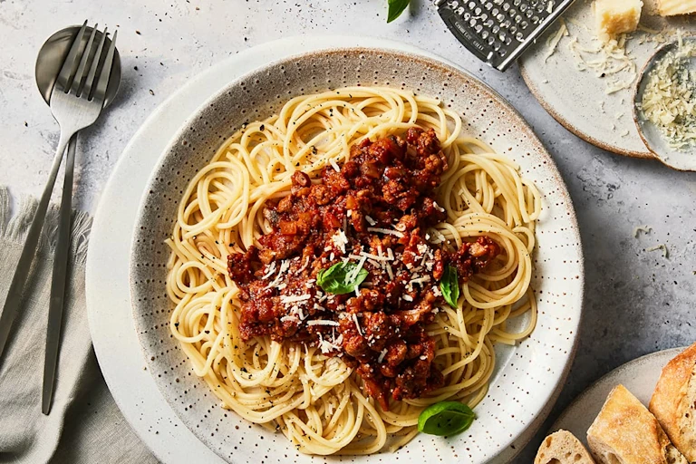 A bowl of spaghetti Bolognese made with Quorn Grounds topped with basil and Parmesan cheese.