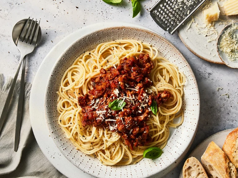 A bowl of spaghetti Bolognese made with Quorn Grounds topped with basil and Parmesan cheese.