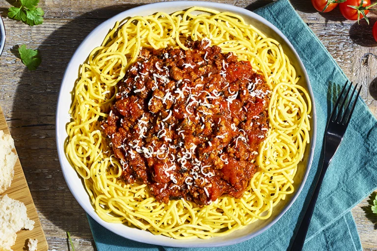 A bowl of spaghetti Bolognese made with Quorn Grounds topped with basil and Parmesan cheese.