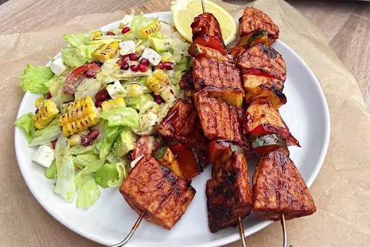 Three Quorn Vegetarian BBQ Skewers and a side of citrus corn salad served on a white dish.