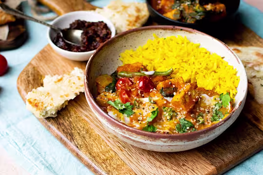 A vegan Jalfrezi curry made with Quorn Vegan Pieces and assorted vegetables topped with yoghurt and coriander served alongside yellow pilau rice in a white bowl.