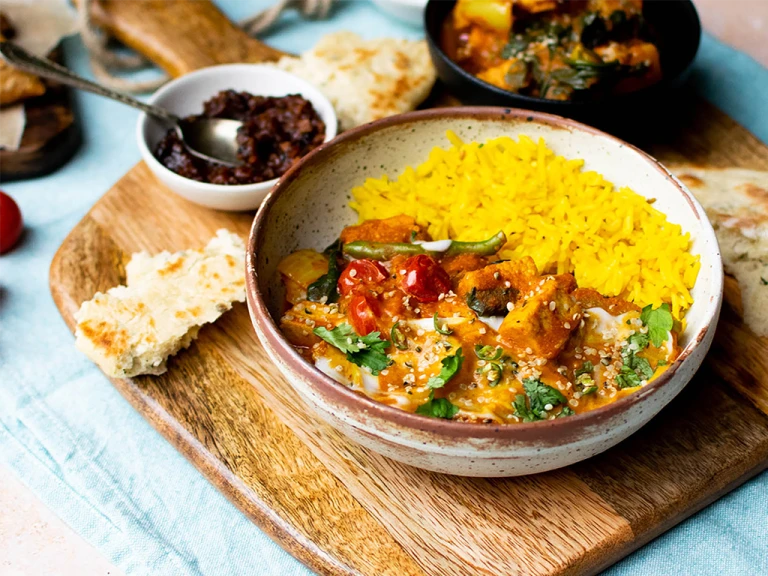 A vegan Jalfrezi curry made with Quorn Vegan Pieces and assorted vegetables topped with yoghurt and coriander served alongside yellow pilau rice in a white bowl.