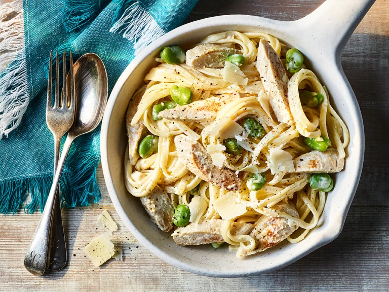Creamy Crème Fraiche Pasta with Quorn Meatless Chicken Fillets served in a white dish with a fork and spoon on the side.