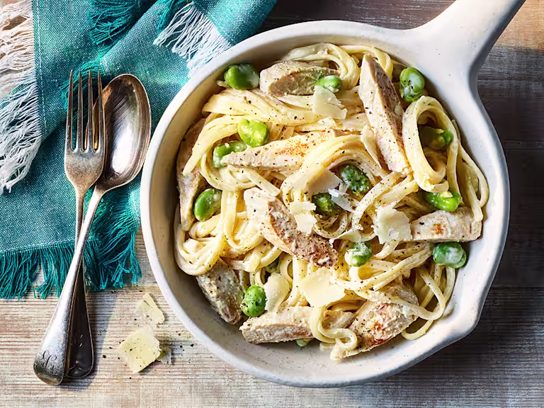 Creamy Crème Fraiche Pasta with Quorn Meatless Chicken Fillets served in a white dish with a fork and spoon on the side.