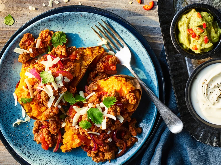 Quorn grounds tinga with sweet potatoes served on a blue dish with guacamole and sour cream on the side.