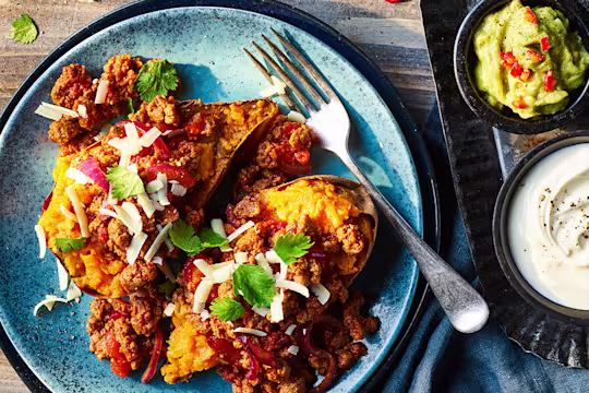 Quorn mince tinga with sweet potatoes served on a blue dish with guacamole and sour cream on the side.