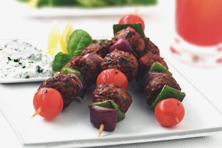 Three kebabs stacked with Quorn Meatballs, cherry tomatoes, green peppers, and red onions with a small dish of yogurt sauce on the side.